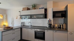 Moderni keittiö, jossa on valkoiset kaapit, sisäänrakennettu uuni, mikroaaltouuni ja pesuallas. Työtasolla on koriste-esineitä, kuten kulho, kasvi ja kahvinkeitin.