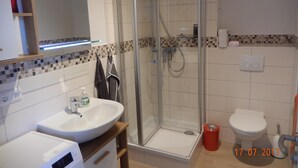 Un baño moderno con ducha de vidrio, lavamanos blanco y retrete.
