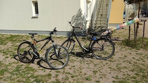 Dos bicicletas estacionadas sobre un terreno de grava frente a un edificio con escaleras y una ventana.