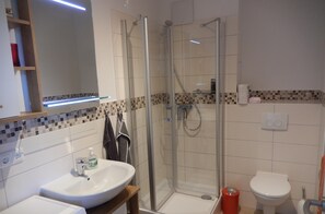 A modern bathroom with a glass-enclosed shower, a white sink, and a toilet.