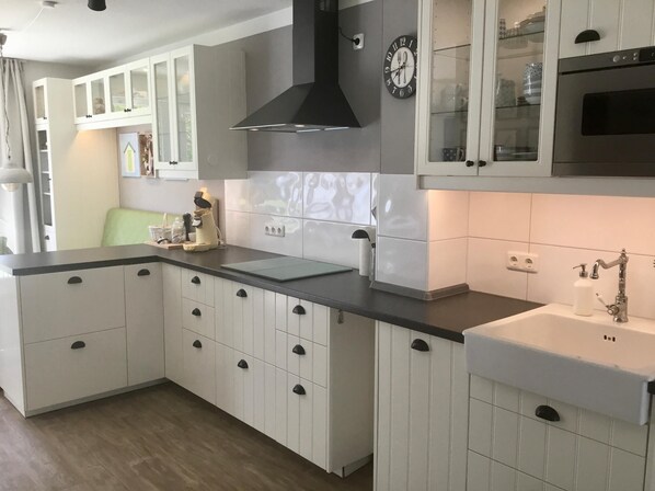 A modern kitchen with white cabinets, a black range hood, a clock, and a built-in oven.