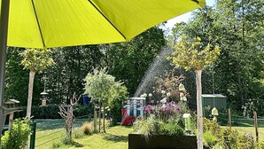 En have med en gul parasol, forskellige planter og en springvand.