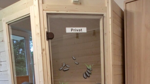 Een houten kast met een glazen deur waarop 'Privat' staat. Binnenin zijn planken met decoratieve stenen en kleine planten.