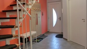 Een trap met een witte leuning, een houten deur met een rondlicht en een zwarte mat op de vloer.