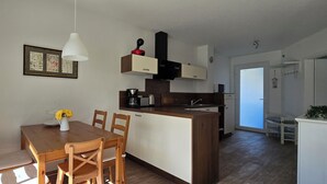 Eine moderne Küche mit Holzausstattung, einer weißen Pendelleuchte und einem Essbereich mit Holztischen und einer Tischplatte.
