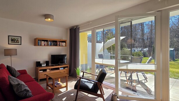 Ein Wohnzimmer mit einem roten Sofa, einem Fernseher, einem Bücherregal und einem Essbereich mit Tisch und Stühlen.
