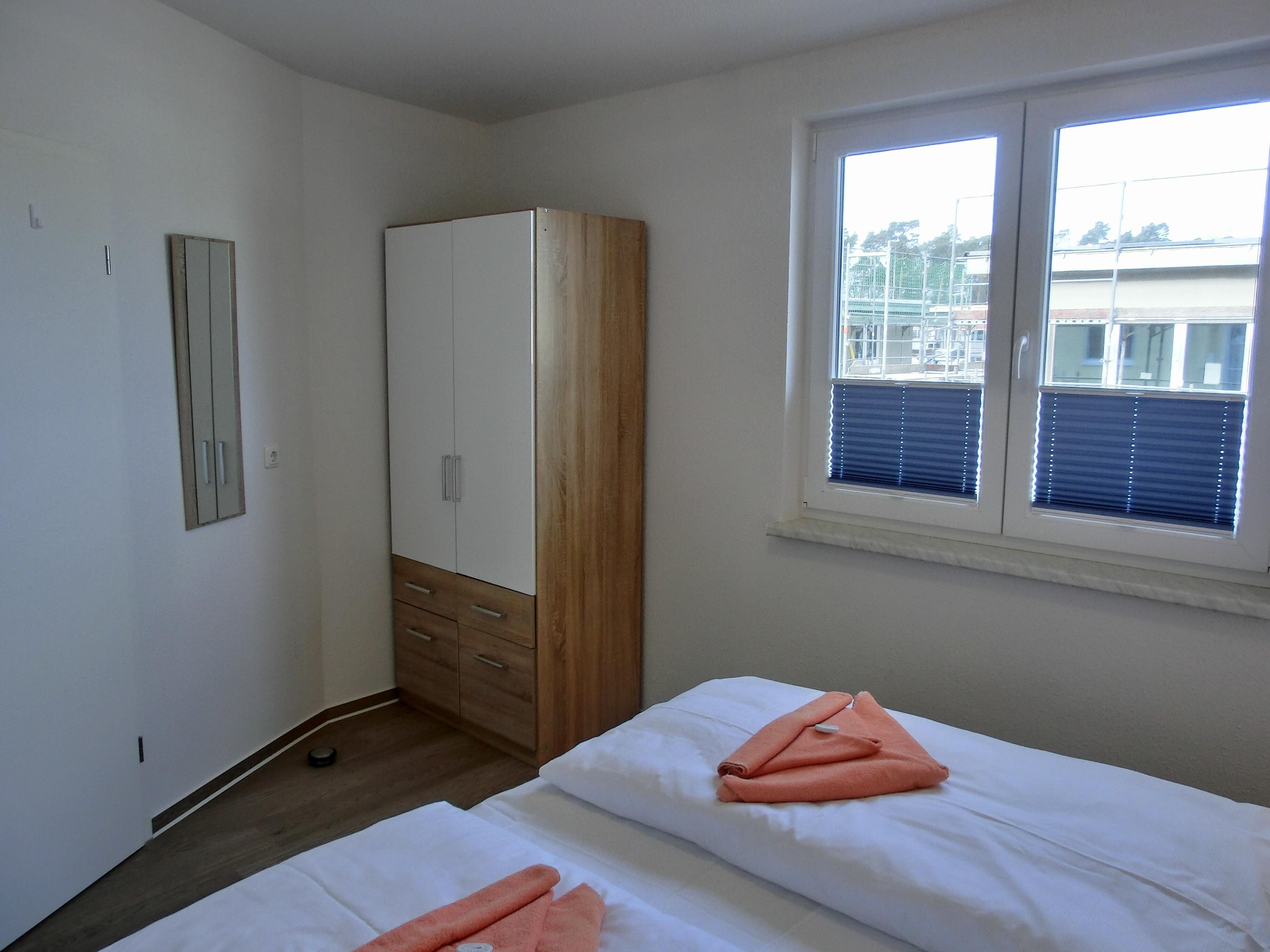 Un dormitorio con dos camas, un armario, una ventana con persianas y un espejo en la pared.