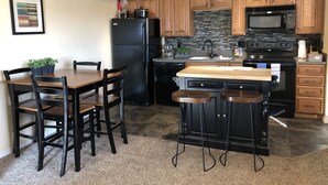 A kitchen with wooden cabinets, a black refrigerator, a microwave, a stove, a sink, and a bar area with stools. - Spacious 1 Bedroom Condo With Cute Bonus Room (St. George)