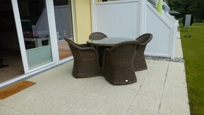 Un patio exterior con mobiliario de mimbre y un ventanal que da a un espacio interior.