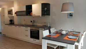 Una cocina moderna con armarios blancos, horno empotrado y comedor con una mesa dispuesta para cuatro.