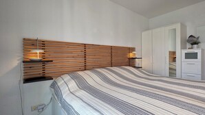 Une chambre à coucher avec une tête de lit en lattes de bois, une couvre-lit à rayures, des lampes de chevet, une armoire et une petite plante en pot.