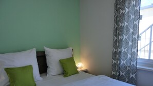 A bed with white and green pillows, a bedside lamp, and a window with patterned curtains. - 2-zimmer-fewo für 2 Pers. im EG mit 2 Fahrrädern (Graal-Müritz)