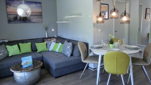 A modern living room with a grey sofa, green and white cushions, a round coffee table, and a dining area with a white table and yellow chairs. - 2-zimmer-fewo für 2 Pers. im EG mit 2 Fahrrädern (Graal-Müritz)