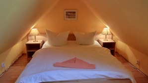 A bedroom with a sloped ceiling, two bedside lamps, a bed with white bedding, and a framed picture on the wall.