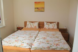 Uma cama de casal com roupa de cama florida, uma mesinha de cabeceira, uma luminária e um quadro na parede.