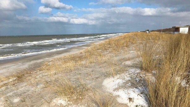 Une plage avec des dunes de sable et un petit bâtiment visible au loin.