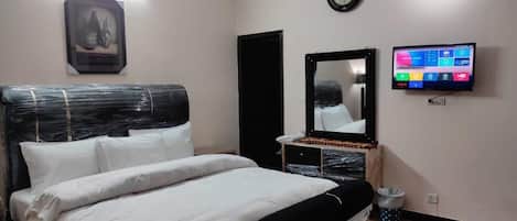 A bedroom with a bed, a TV, a clock, and a framed picture on the wall.
