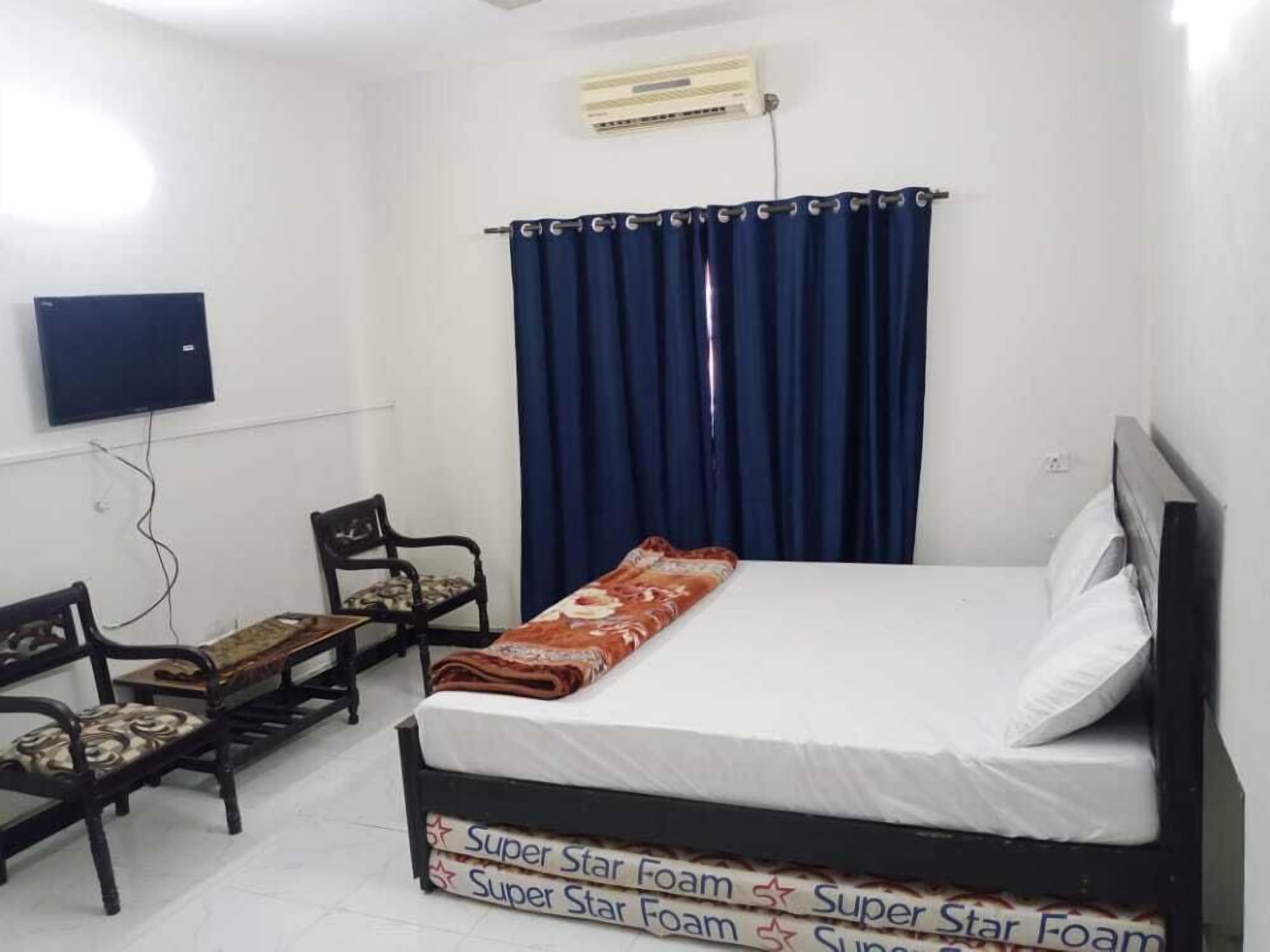 A bedroom with a bed, a chair, a television, and an air conditioning unit.