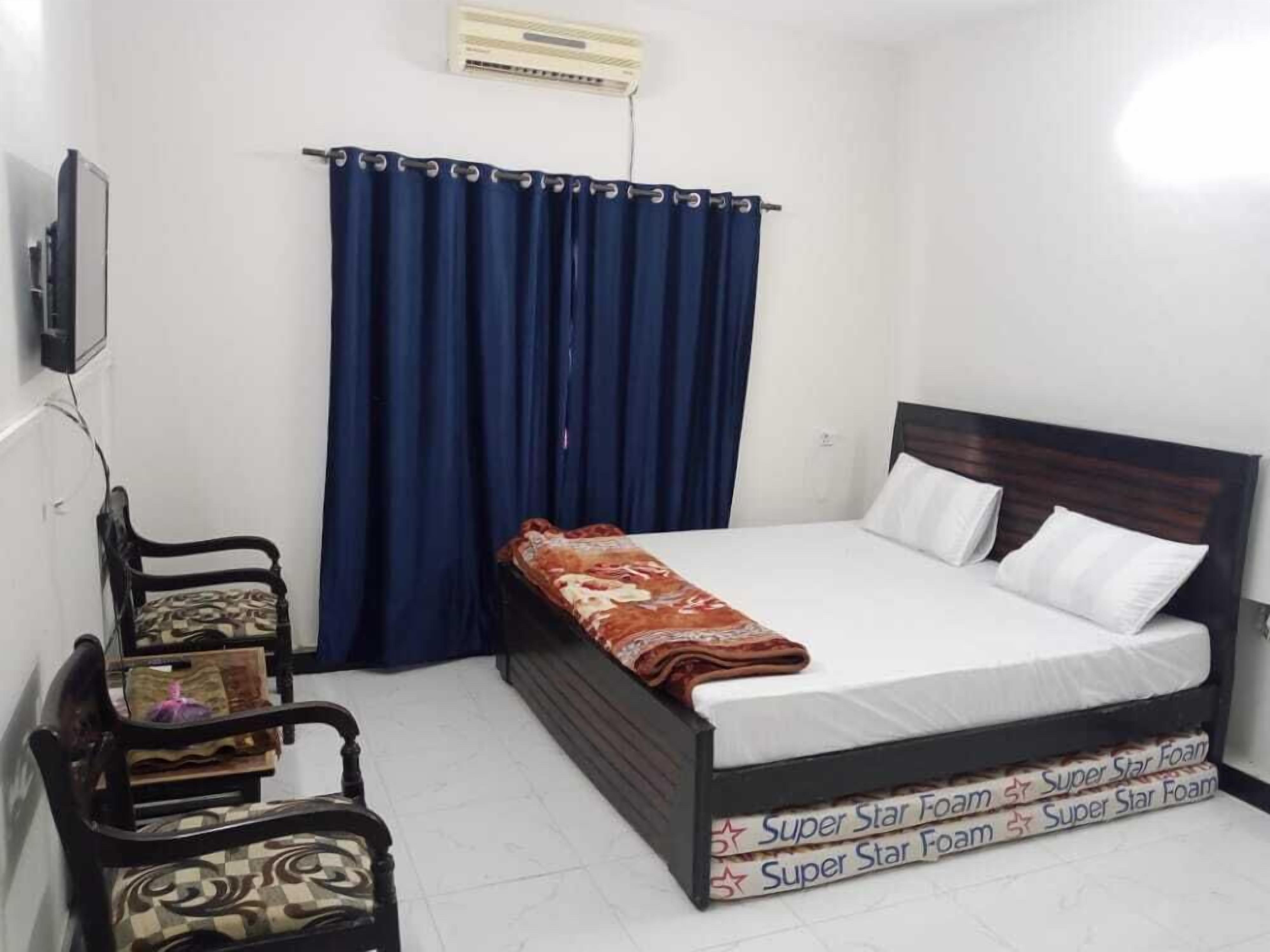 A bedroom with a bed, a chair, a curtain, and an air conditioning unit.