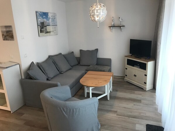 Un salon moderne avec un canapé d’angle gris, une table basse en bois, un téléviseur posé sur un meuble et un luminaire en forme de globe.