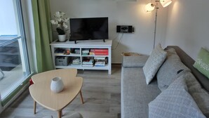Ein modernes Wohnzimmer mit Flachbildfernseher, Bücherregalen, einer Couch und einer Stehlampe.