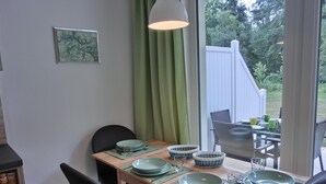 Ein Essbereich mit einem Holztisch, gedeckten Plätzen für vier Personen, grünen Tellern und Blick auf den Garten durch ein Fenster.