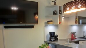 Et moderne køkken med et fladskærms-TV, kaffemaskine og et spiseområde med et bord dækket til to.