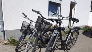Dos bicicletas estacionadas en un área pavimentada frente a un edificio de fachada blanca y una ventana con cortina azul.