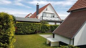 Un jardín bien cuidado con césped, un banco de madera y un edificio blanco con techo de tejas rojas.