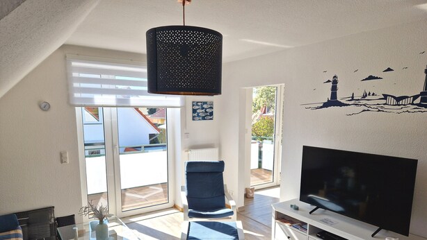 Una sala de estar moderna con televisor, una mesa de centro de vidrio, un sillón azul y un ventanal grande.