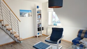 Una sala de estar moderna con una escalera, una estantería, un sillón azul y una mesa de centro de vidrio.