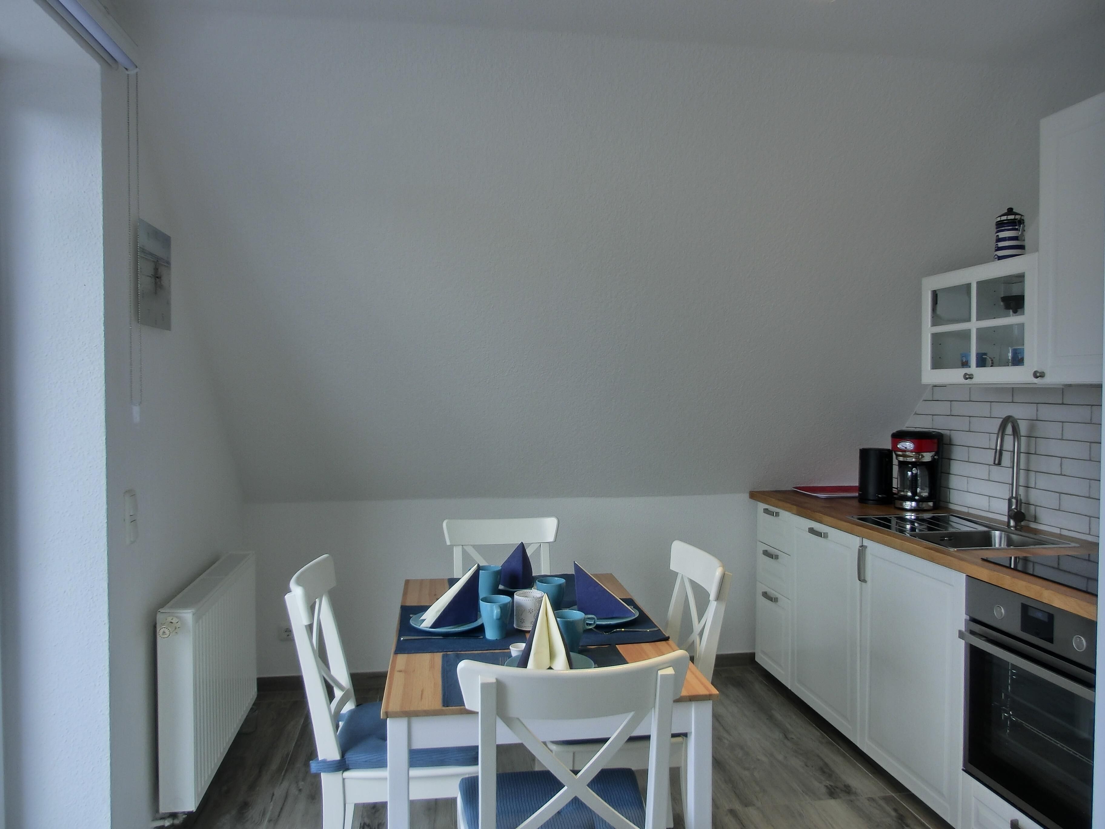 A compact kitchen with white cabinets, a wooden countertop, and a dining area with a table and chairs.