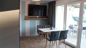 Un espace repas moderne avec une grande table et des chaises, un téléviseur à écran plat fixé au mur et une porte-fenêtre coulissante donnant sur un patio extérieur.