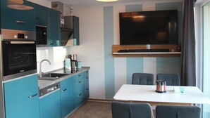 Une cuisine moderne équipée d’un four, d’un micro-ondes et d’un évier intégrés. On y trouve une table à manger avec des chaises, et un téléviseur à écran plat fixé au mur au-dessus de la table.