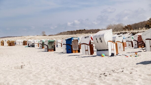 Beach huts with numbers on them, arranged in a row on a sandy beach. - Beachfront 3-room apartment for 5 people with WiFi and wallbox (Graal-Müritz)