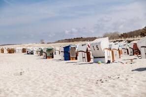 Beach huts with numbers on them, arranged in a row on a sandy beach.