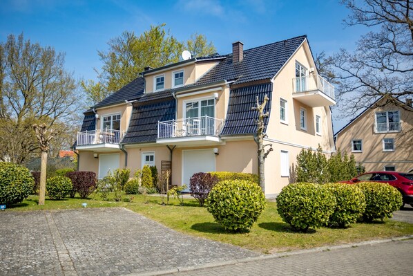 A two-story house with a balcony, a driveway, and well-maintained hedges.