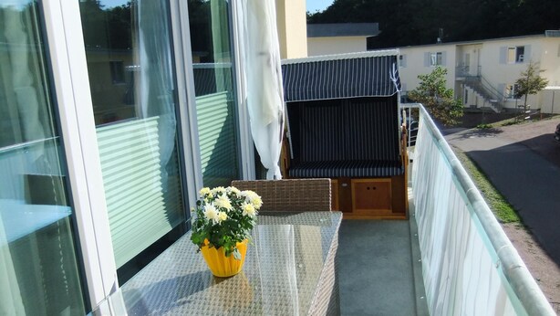 A balcony with a glass table, a wicker bench, and a yellow flower vase. - 2-zimmer-fewo für 3 Pers. im OG mit Wlan (Graal-Müritz)