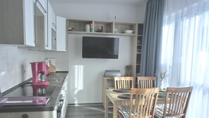 A modern kitchen with a dining area, wooden chairs, and a flat-screen TV mounted on the wall. - 2-zimmer-fewo für 3 Pers. im OG mit Wlan (Graal-Müritz)