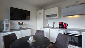 A compact kitchen with a dining area, a flat-screen TV, a coffee maker, and a microwave. - 2-zi.-fewo für 3 Pers. im EG und Gartenanteil (Graal-Müritz)