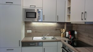 A modern kitchen with white cabinets, a built-in microwave, a sink, a dishwasher, and a stove. - 2-room apartment for 3 people close to the beach (Graal-Müritz)