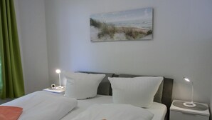 A hotel room with two beds, a bedside table with a lamp, a nightstand, a green curtain, and a painting on the wall. - 2-room apartment for 3 people close to the beach (Graal-Müritz)