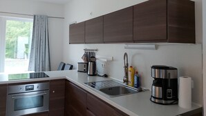 Eine moderne Küche mit Edelstahlgeräten, einem eingebauten Ofen, einer Kaffeemaschine und einem Fenster mit Vorhängen.
