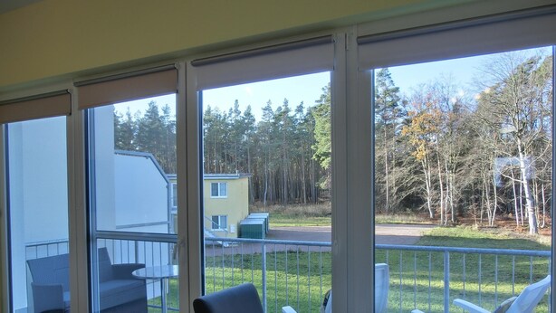 Ein Essbereich mit Tisch für zwei Personen, großen Fenstern und Blick auf eine bewaldete Landschaft.