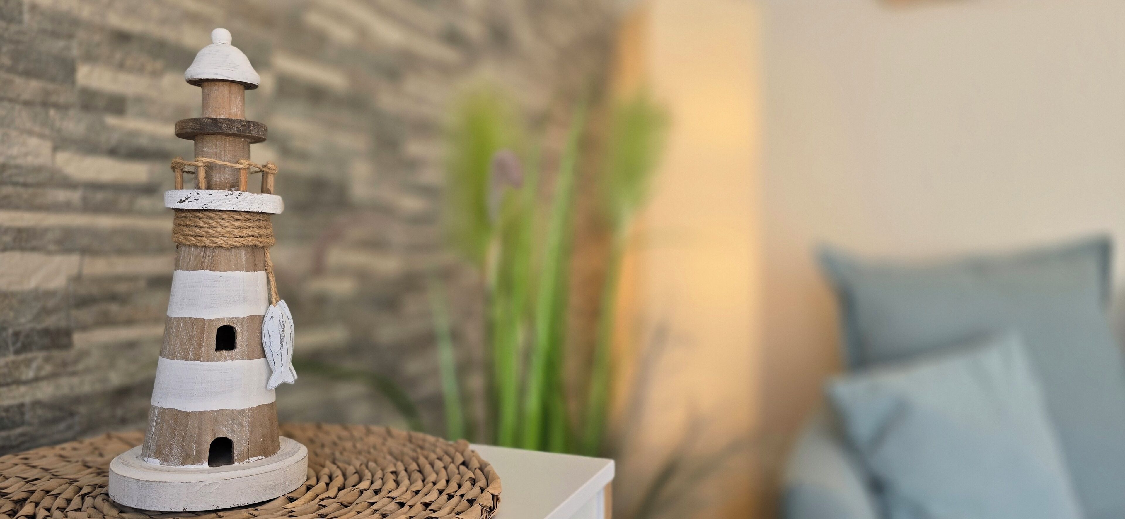 A lighthouse model on a woven mat, with a stone wall and a blue pillow in the background.