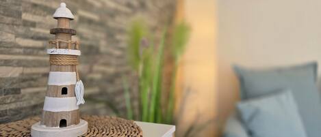 A lighthouse model on a woven mat, with a stone wall and a blue pillow in the background.