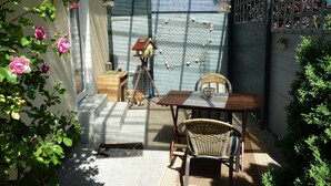 Un pati il·luminat pel sol amb una taula de fusta, cadires de vímet, un gos petit i un niu d'ocell.