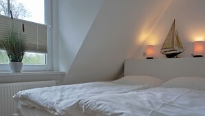 Ein Schlafzimmer mit einem Bett, einem Fenster mit Jalousien, einer Heizung und einer Zimmerpflanze.
