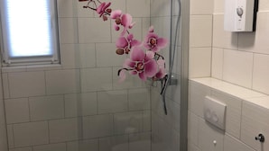 Ein Badezimmer mit weißen Fliesenwänden, einer Duschkabine aus Glas, einer Toilette und einem Waschbecken.