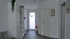 Ein Flur mit einer weißen Tür, einem kleinen Tisch, einem roten Stuhl und einer Pflanze an der Wand.